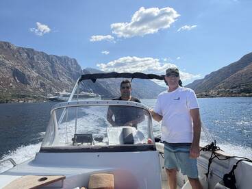 Two men enjoy a scenic boat ride with stunning mountain views in the background, perfect for exploring coastal destinations.