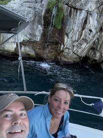A couple enjoys a scenic moment on their boat with a beautiful waterfall in the background, capturing a perfect selfie during their adventure.