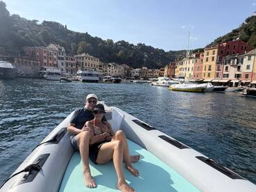 A couple relaxes on a boat in a picturesque harbor, surrounded by colorful buildings and serene waters — a perfect setting for a romantic getaway.