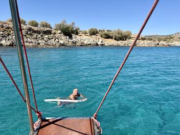 A man enjoys a refreshing swim in crystal-clear waters near a rocky coastline, showcasing the beauty of outdoor adventures on the water.