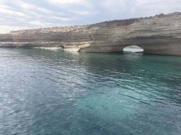 A stunning view of a natural rock arch along the coastline, surrounded by clear turquoise waters — a perfect destination for boat tours and scenic explorations.