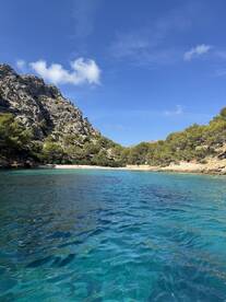 A stunning view of a secluded beach surrounded by rocky cliffs and lush greenery, showcasing the crystal-clear waters — an ideal destination for a relaxing day on the water.