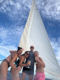 A joyful group celebrates aboard a sailboat, raising glasses of champagne against a backdrop of blue skies and billowing sails — perfect for memorable sailing adventures.