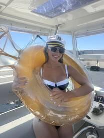 A smiling woman in a captain's hat poses with a fun float on a boat, capturing the essence of a joyful day on the water.