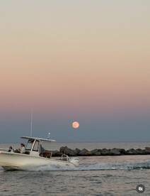 A scenic view of a boat cruising at sunset with a full moon rising in the background, capturing the essence of a perfect evening on the water.