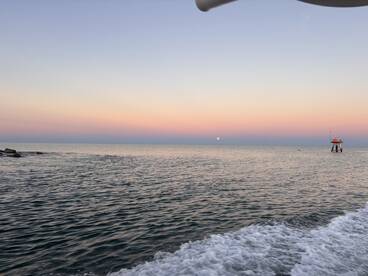 A serene sunset view over calm waters, showcasing the beauty of nature as the moon rises on the horizon — perfect for tranquil boating experiences.