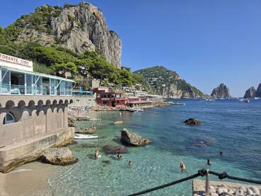 A vibrant beach scene on the island of Capri, showcasing people enjoying the crystal-clear waters and stunning coastal views — a perfect destination for sun-seekers and adventurers.