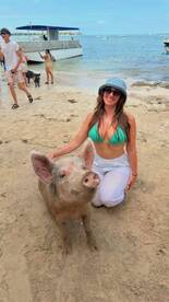 A woman interacts with a friendly pig on the beach, showcasing a unique wildlife experience that highlights the charm of swimming pigs in tropical destinations.