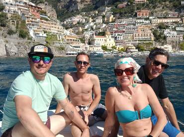 A cheerful group enjoys a sunny day on a boat, with a stunning coastal backdrop — perfect for memorable outings along the Amalfi Coast.