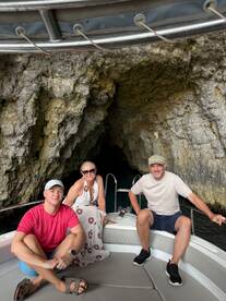 A group of friends relaxes on a boat near a stunning cave entrance, perfect for exploring the natural beauty of coastal landscapes.