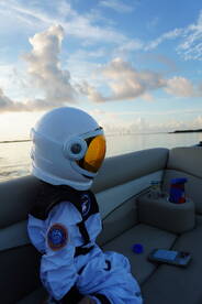 A child dressed as an astronaut enjoys a serene moment on a boat during sunset, capturing a whimsical blend of adventure and tranquility on the water.