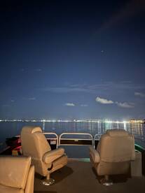 Interior view of a pontoon boat at night, showcasing comfortable seating and a serene reflection on the water, perfect for evening cruises.