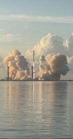 A rocket launch is captured against a backdrop of clouds and water, showcasing a dramatic scene of technology and nature.