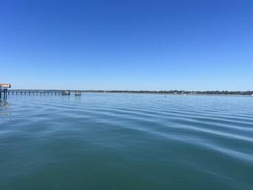 A serene view of calm waters and a distant pier under a clear blue sky, perfect for capturing the tranquility of a day on the water.
