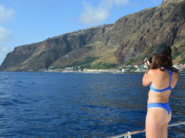 A woman captures the stunning coastline with her camera while enjoying a boat trip, showcasing the beautiful landscape and vibrant blue waters.