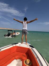 A person stands triumphantly at the bow of a boat, arms outstretched, enjoying the beautiful ocean view — a perfect moment of freedom and adventure on the water.