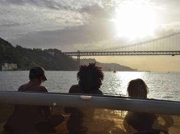 A group of friends enjoys a serene sunset view from their boat, with a stunning bridge in the background — perfect for memorable moments on the water.