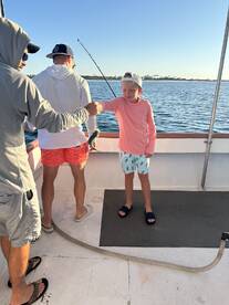 A young boy proudly holds up a fish while fishing with adults on a boat, capturing a memorable family experience on the water.