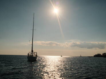 A serene view of a sailboat gliding through shimmering waters under a bright sun, perfect for showcasing tranquil sailing experiences.