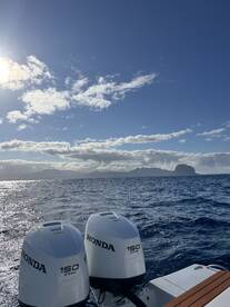 A clear view of outboard motors on a boat, with stunning ocean scenery and distant islands under a bright sky — perfect for showcasing boating adventures.