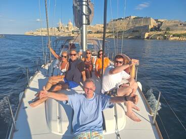 A lively group enjoys a sunny day aboard a yacht in Malta, celebrating with drinks and smiles against a stunning coastal backdrop.