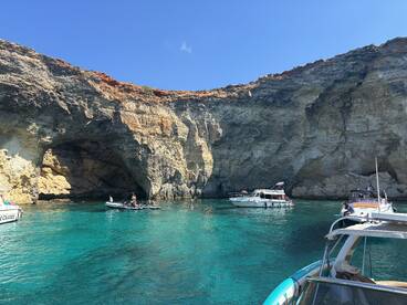 A vibrant scene of boats anchored near a stunning cave, with people enjoying the crystal-clear waters — a perfect spot for swimming and exploration.