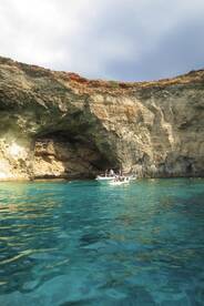 A scenic view of a boat near a stunning cave in Malta, with swimmers enjoying the crystal-clear waters — a perfect spot for adventure and exploration.