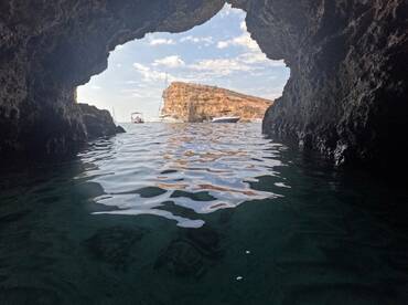 A stunning view from inside a cave looking out towards boats anchored near a rocky island, showcasing the beauty of coastal scenery.