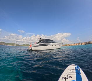 A scenic view of a yacht with guests enjoying the sun, while a paddleboarder approaches — a perfect snapshot of a fun day on the water.