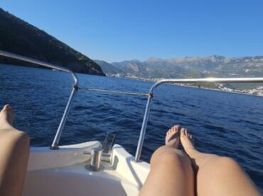 A serene moment on a boat with feet resting on the bow, showcasing stunning mountain scenery and calm waters — perfect for relaxation and enjoying the views.