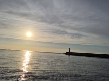 A serene view of the sun setting over calm waters, with a distant pier visible. This tranquil scene captures the beauty of a peaceful evening on the water.