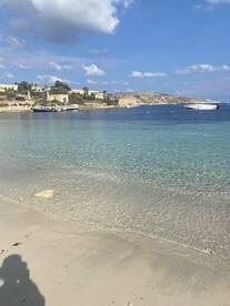 A serene view of a clear beach with boats anchored in the distance, showcasing the beautiful coastline and tranquil waters — perfect for a relaxing getaway.