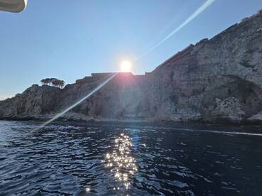 A stunning sunset casts a warm glow over the rocky coastline, creating a picturesque scene perfect for boat trips and coastal explorations.