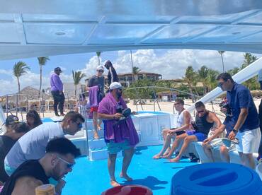 A lively group enjoys their time aboard a boat, with drinks in hand and the beach in the background — perfect for a fun day on the water.