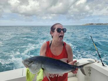 A thrilled angler proudly displays her catch while out on the ocean, capturing the excitement of a successful fishing trip.