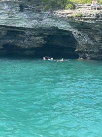 A group of friends enjoys swimming near a rocky cave in crystal-clear waters, perfect for snorkeling adventures and exploring hidden gems.