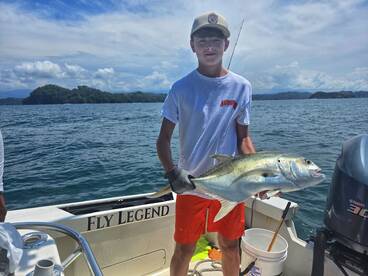 A young angler proudly displays his catch aboard the 'Fly Legend' boat, showcasing the excitement of fishing in beautiful waters.