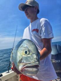 A young angler proudly holds up a freshly caught fish while out on the water, showcasing the excitement of fishing adventures.