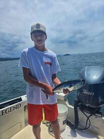 A young boy proudly holds up his catch while fishing on a boat, showcasing the excitement of a successful day on the water.