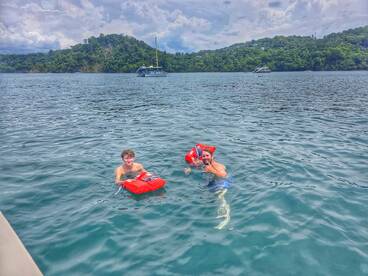 Two young swimmers enjoy a fun day in the water, showcasing their life jackets while surrounded by beautiful scenery — perfect for family adventures and water activities.
