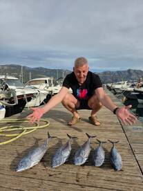 A proud angler showcases his impressive catch of fish at the dock, celebrating a successful fishing trip amidst a scenic marina backdrop.