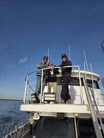 A cheerful group poses on the deck of a fishing boat, enjoying a beautiful day on the water — perfect for fishing trips and memorable outings.