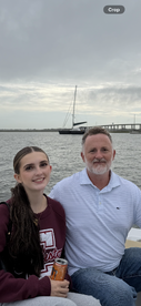 A couple poses for a photo on a boat with a scenic backdrop of water and a sailboat in the distance, capturing a memorable moment on their boating adventure.