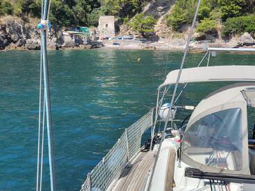 A serene view of a sailboat anchored near a rocky shore, showcasing the beautiful turquoise waters and surrounding greenery.