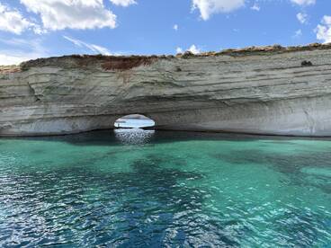 A stunning view of a natural rock arch with crystal-clear waters, showcasing the beauty of the coastline — perfect for exploring hidden gems while boating.