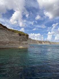 A picturesque view of a sailboat anchored near stunning cliffs and clear waters, perfect for island hopping adventures.