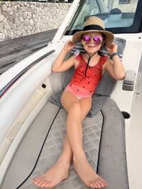 A young girl relaxes in a stylish cabin area of a boat, wearing a playful watermelon swimsuit and sunglasses, perfect for a fun day on the water.