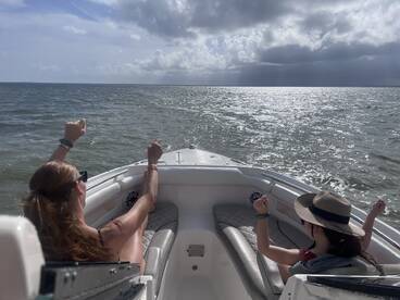Two friends enjoy a fun moment on the boat, celebrating under the sun while cruising on the ocean — perfect for memorable outings and adventures.