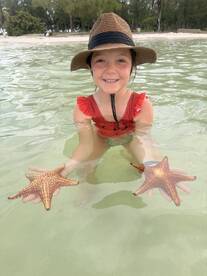 A young girl joyfully holds two starfish while wading in shallow waters, showcasing a delightful wildlife encounter in a tropical paradise.