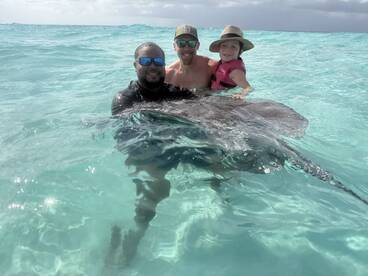 A memorable encounter as a child and two adults interact with a stingray in the clear waters, showcasing the beauty of wildlife experiences in the ocean.